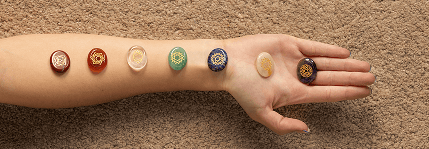 Seven coloured chakra stones laid along a forearm on sand